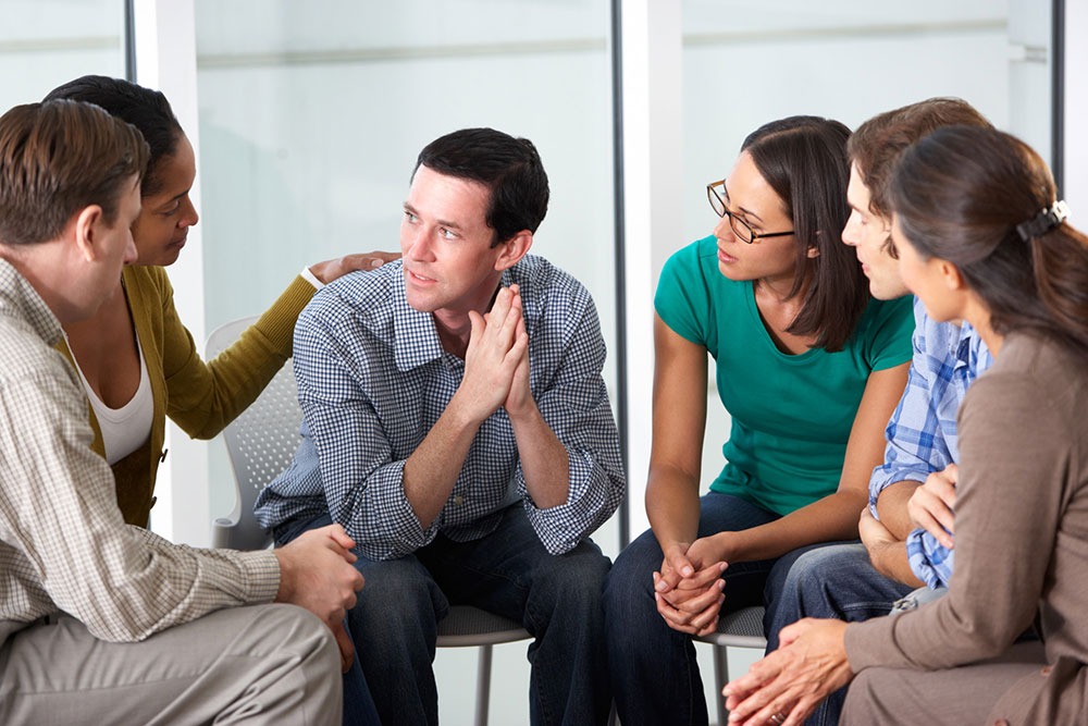 A support group comforting a man during a therapy session for precipitated withdrawal